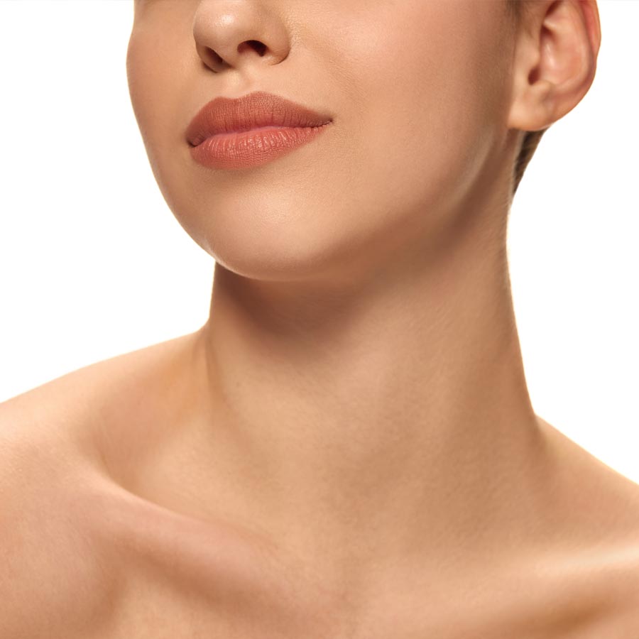 Close-up of young woman's chin and defined jawline with healthy, smooth, lifted skin against white studio background.